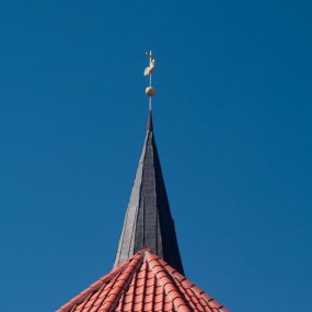 A church spire with a red tiled roof stands against a clear blue sky, highlighting architecture.