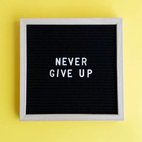 Black felt board with 'Never Give Up' on a bright yellow background for motivation.